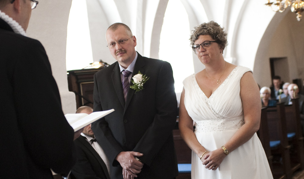 Brudepar står foran præst ved alteret i middelalderkirke ved bryllup i folkekirken